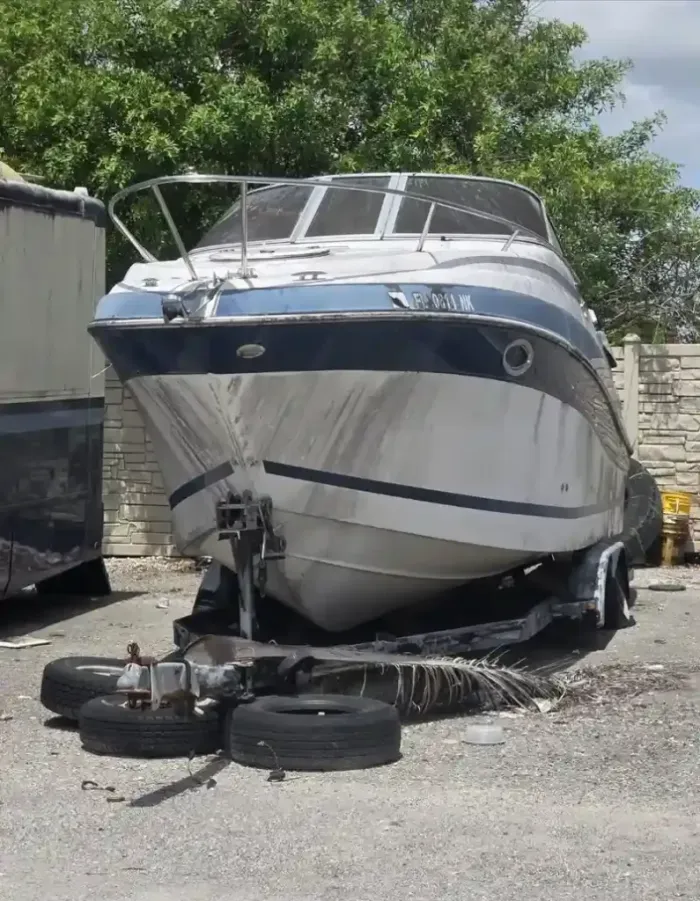 Old deteriorated boat on a towing trailer in a backyard, prepared for removal and disposal